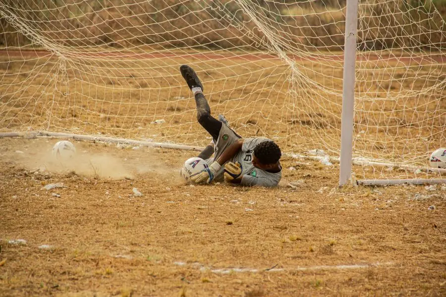 Goalkeeper diving to smother a low ball on a dry pitch