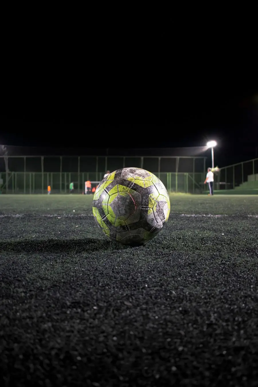 A scuffed football on a floodlit pitch at night